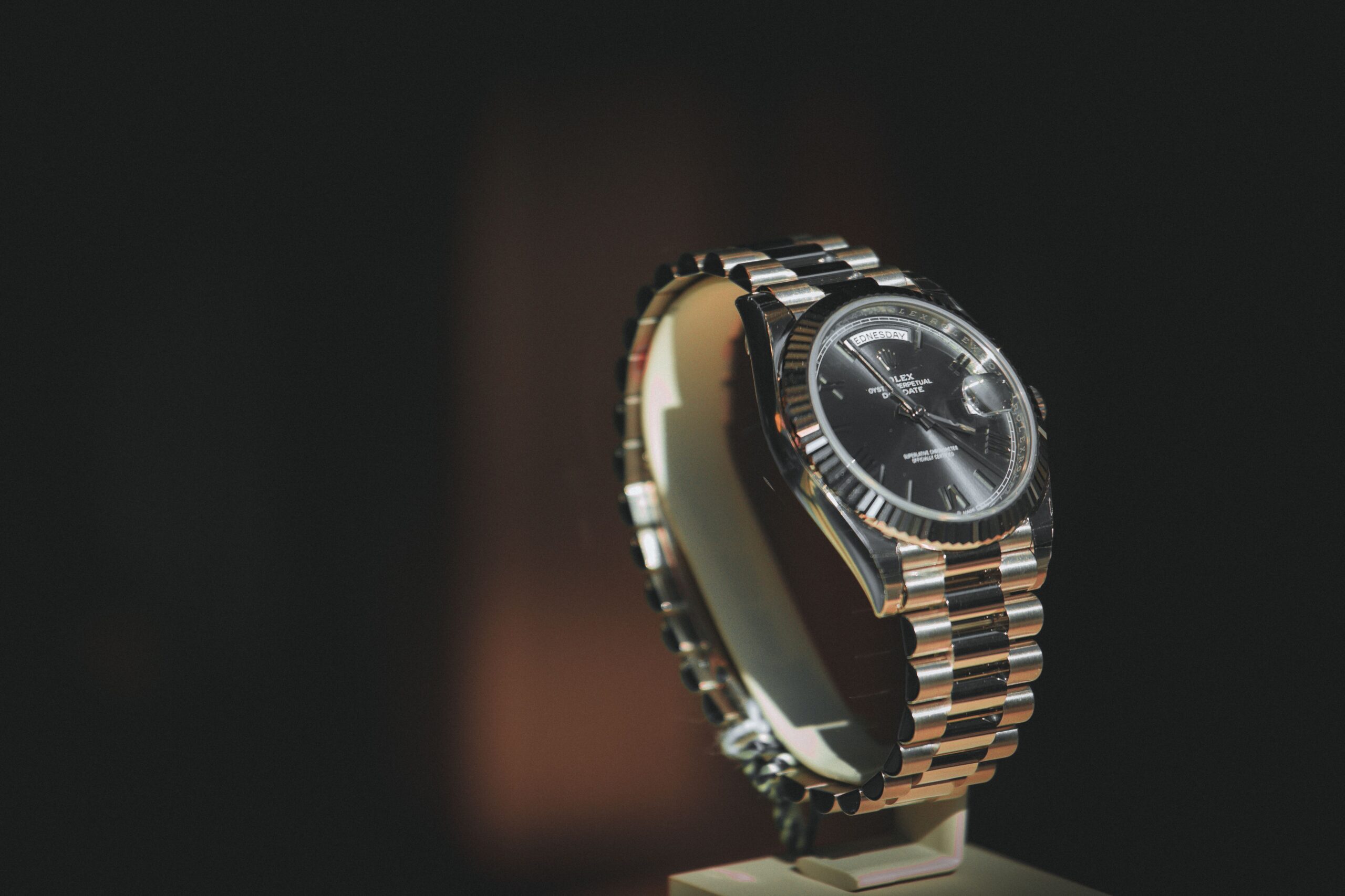 Luxury silver wristwatch displayed on a stand with dark cinematic lighting and blurred background.